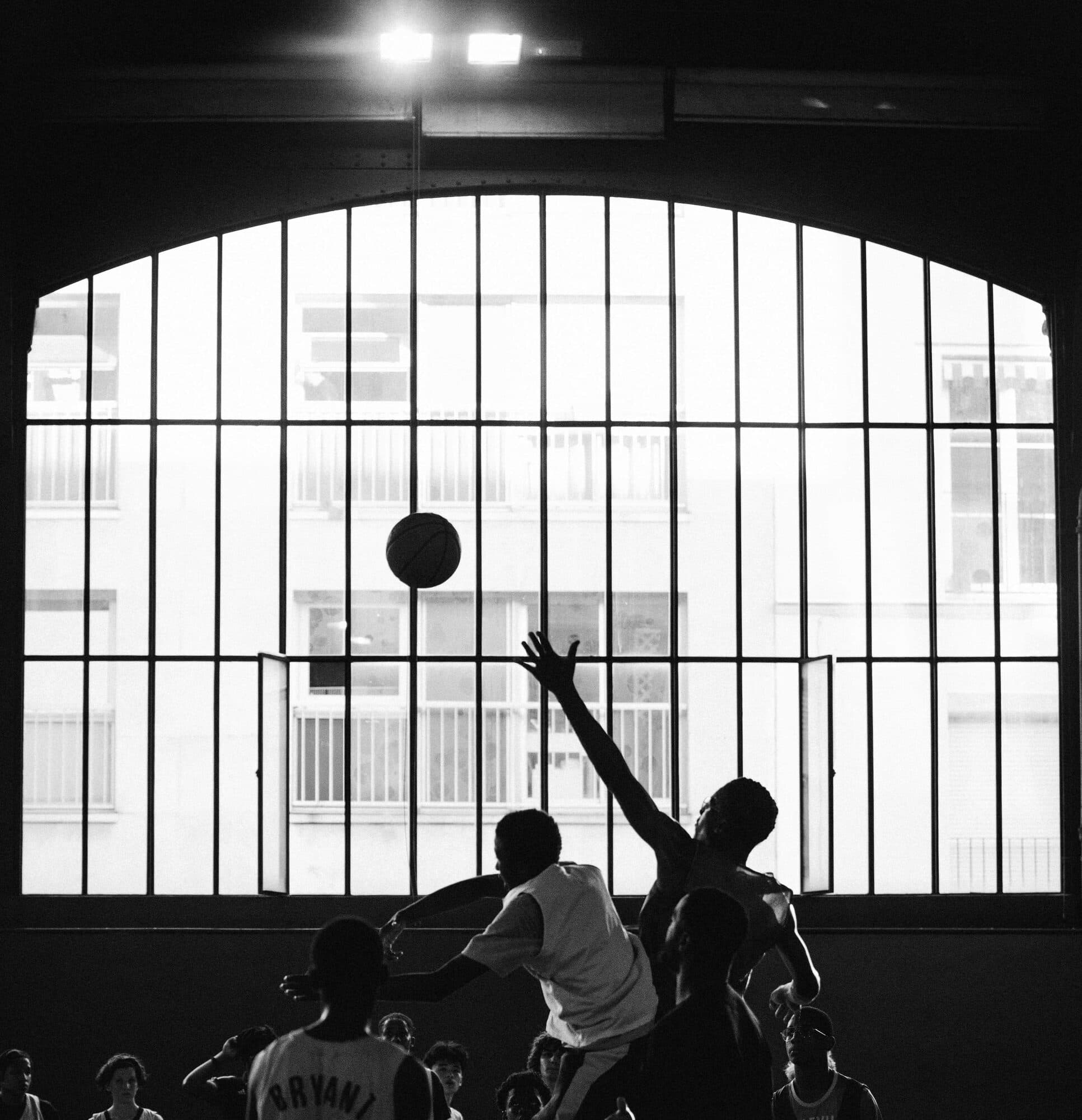 Un joueur au rebond dans le gymnase, à contre-jour de la verrière